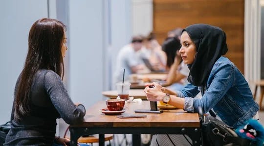 To damer snakker sammen over en kopp kaffe